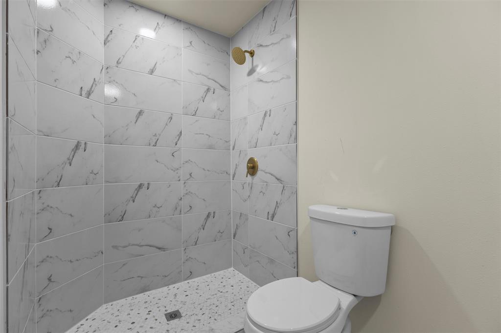 Shower stall with patterned tile wall surround, brass-finish fixtures, and a textured stone-finish shower pan