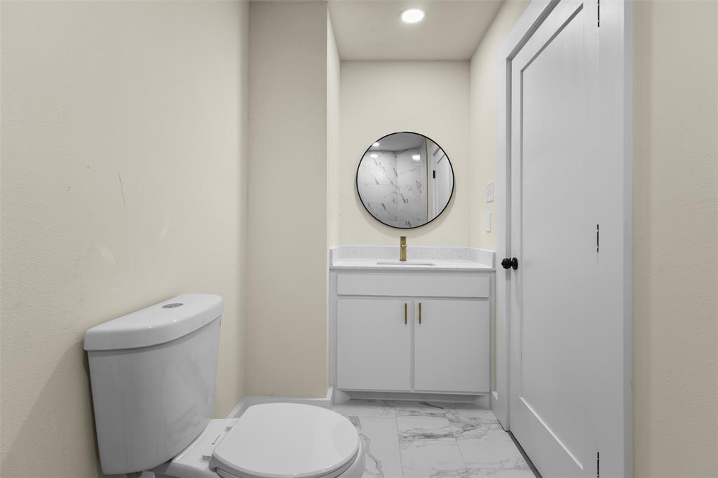 Modern vanity with white cabinetry, stone-finish countertop, undermount sink, and brass-tone hardware, complemented by a round wall-mounted mirror, brass-tone faucet, and stone-patterned tile flooring