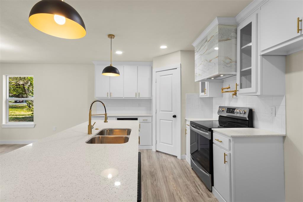 Kitchen featuring white shaker-style cabinetry, quartz countertops, a stone-finish range hood, gold-tone hardware, and wood-finish flooring