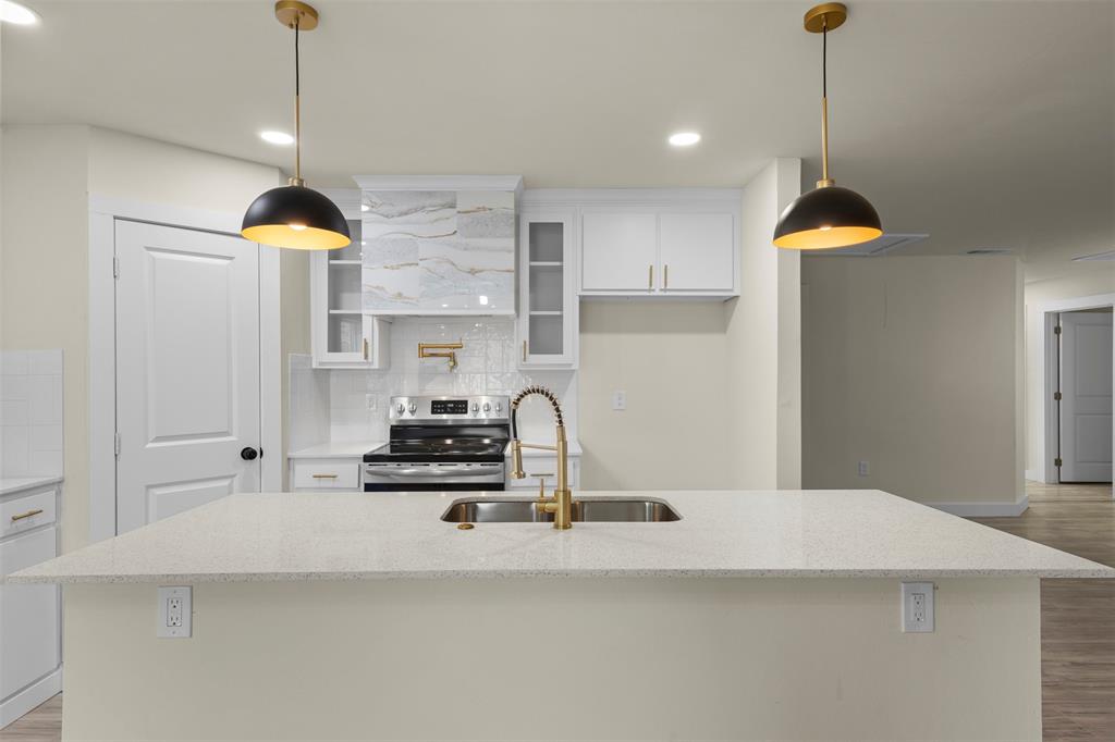 Kitchen featuring a stone-composite countertop island, brass-tone fixtures, custom-milled cabinetry with glass-panel accents, patterned tile range hood surround, and dual dome-style pendant lighting