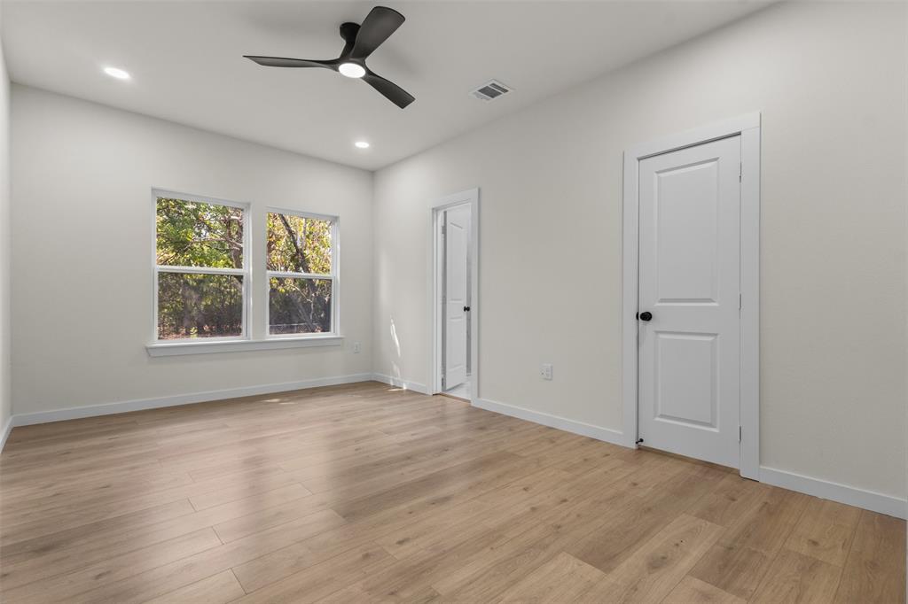Light wood-finish flooring, white walls, and a modern ceiling fan with integrated lighting