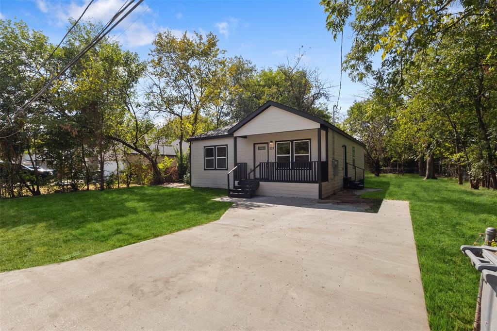 Contemporary exterior with light siding and dark trim, featuring a covered front porch with dark railing, a concrete driveway, and surrounding mature trees Contemporary exterior with light siding and dark trim, featuring a covered front porch with dark railing, a concrete driveway, and surrounding mature trees
