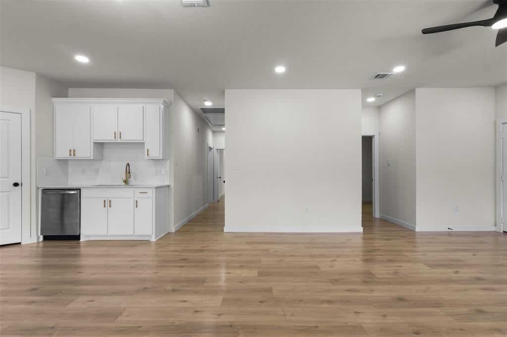Wood-finish flooring, recessed lighting, ceiling fan, white cabinetry with gold-tone hardware, and a stainless steel dishwasher Wood-finish flooring, recessed lighting, ceiling fan, white cabinetry with gold-tone hardware, and a stainless steel dishwasher
