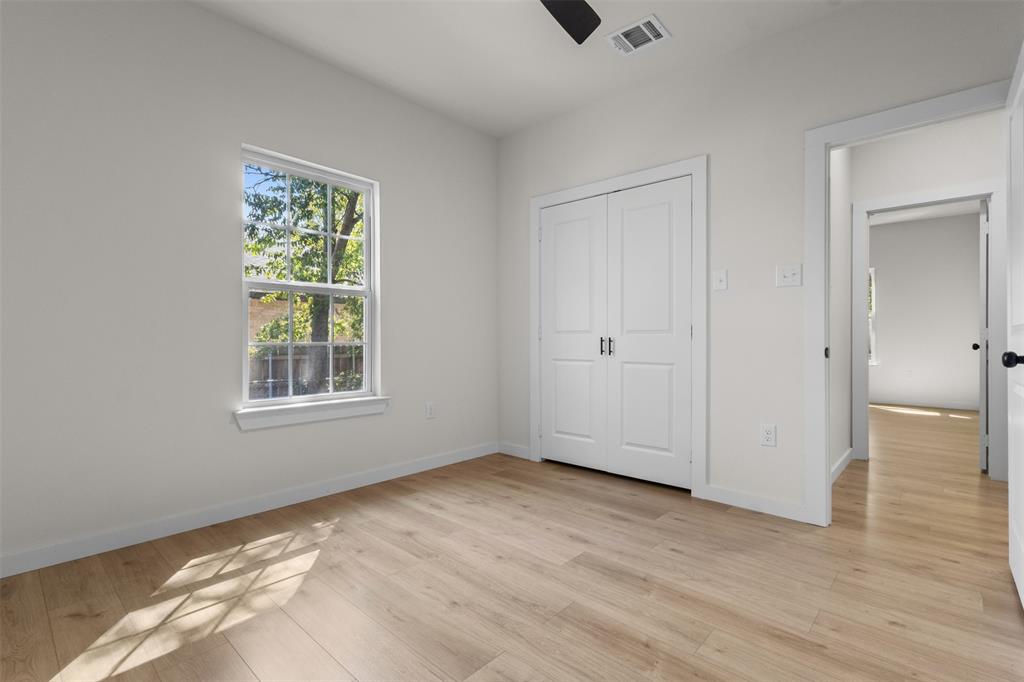 Wood-finish flooring, white walls, double-door closet, window with exterior foliage, and a ceiling fan