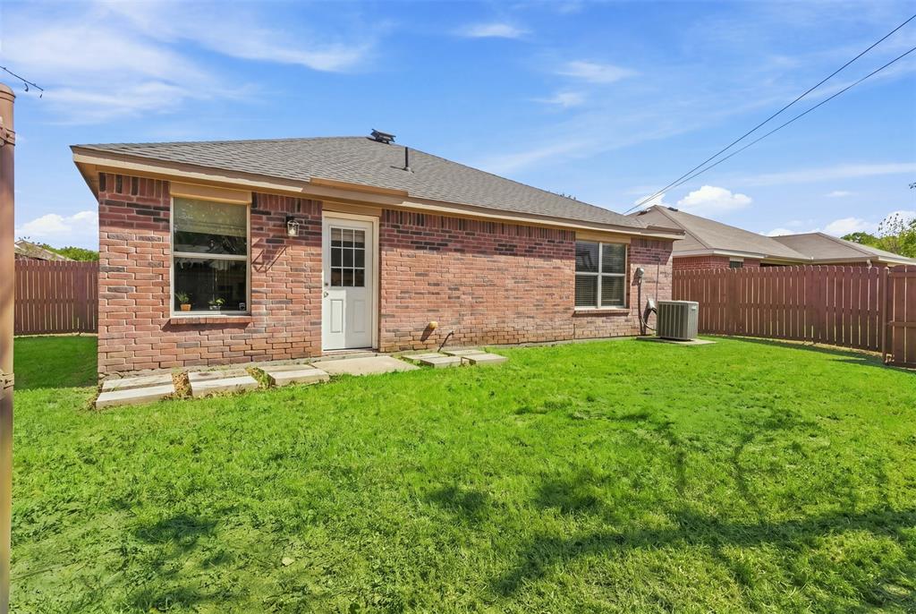 Expansive rear yard featuring a manicured lawn, brick exterior, and full privacy fencing