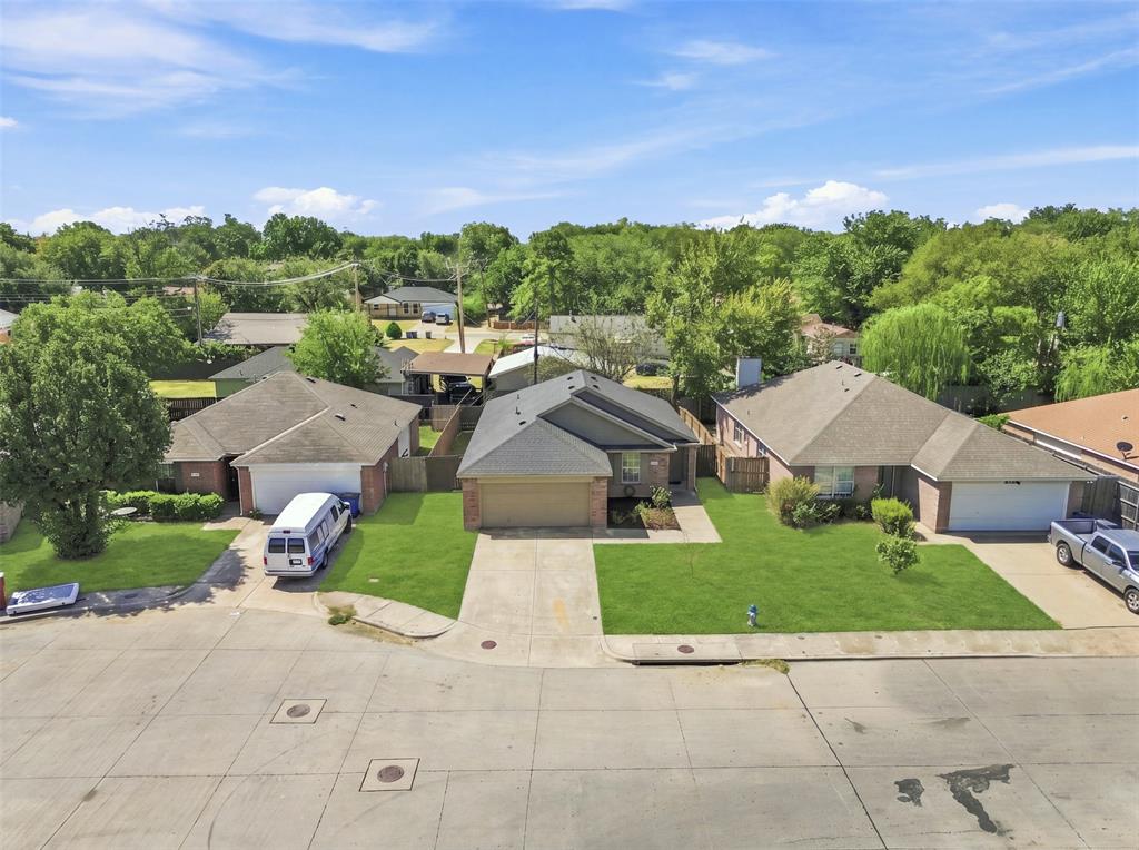 Spacious residential lot featuring a single-story brick home with an attached two-car garage, concrete driveway, and expansive manicured lawn bordered by mature trees