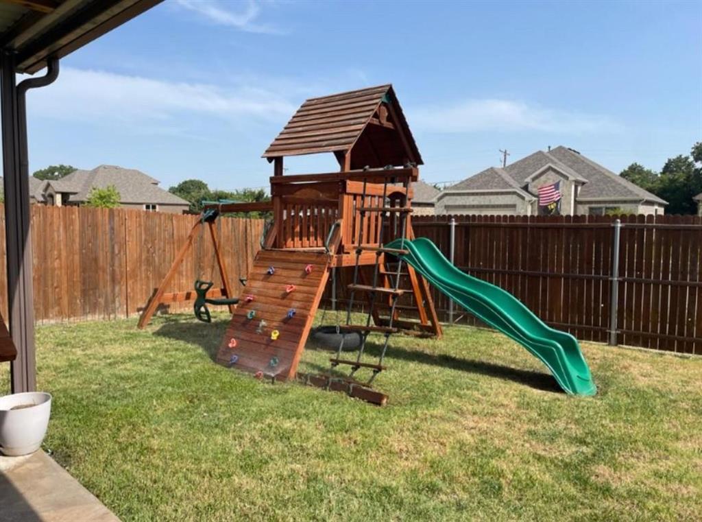 Expansive backyard featuring a wood privacy fence, green lawn, and a multi-level playset with a slide and climbing wall