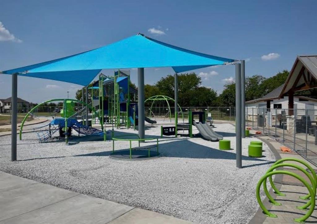 Playground featuring a blue shade structure, multiple play elements, a rubberized safety surface, and a nearby covered pavilion