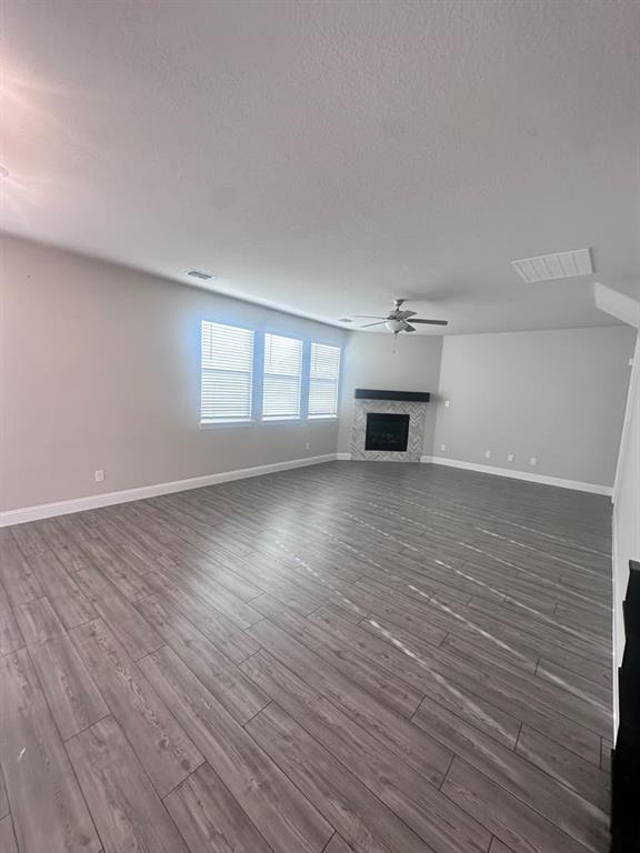Spacious interior with wood-finish flooring, multiple windows with blinds, a ceiling fan, and a fireplace with a mantel Spacious interior with wood-finish flooring, multiple windows with blinds, a ceiling fan, and a fireplace with a mantel