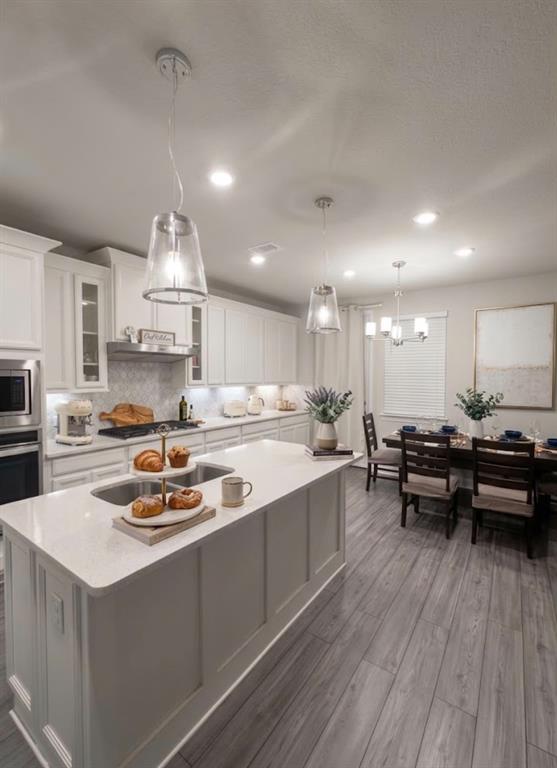 Kitchen with a large island featuring an undermount sink and light-toned countertop, white cabinetry, stainless steel appliances, and a tile backsplash Kitchen with a large island featuring an undermount sink and light-toned countertop, white cabinetry, stainless steel appliances, and a tile backsplash