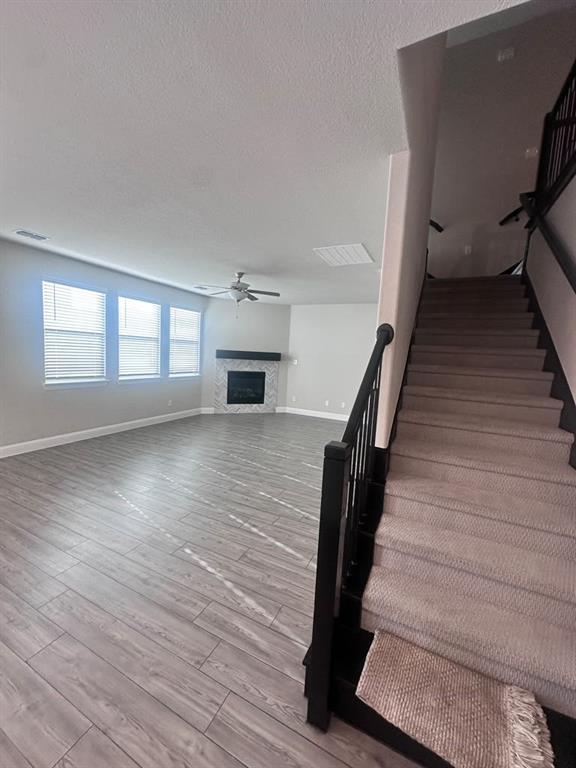 Expansive living area featuring wood-finish flooring, a ceiling fan, and multiple windows with blinds Expansive living area featuring wood-finish flooring, a ceiling fan, and multiple windows with blinds