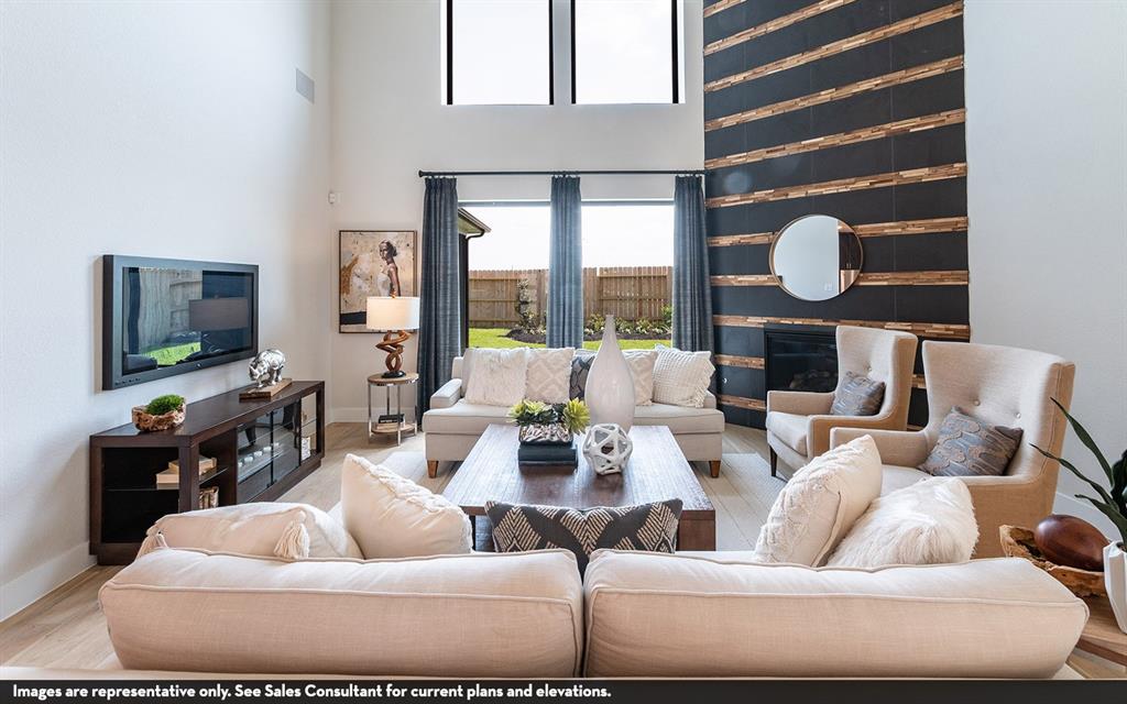 High ceilings, wood-finish flooring, two-story windows, a fireplace with a textured surround, and dark-framed windows