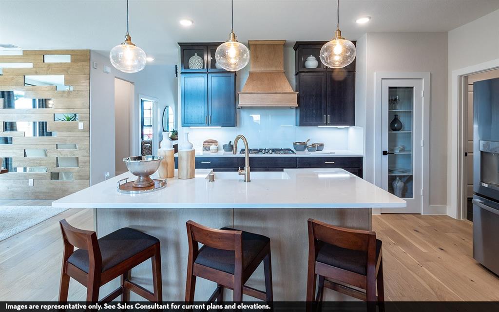Kitchen featuring a large island with a light-toned countertop, wood-finish flooring, dark cabinetry, and three pendant light fixtures