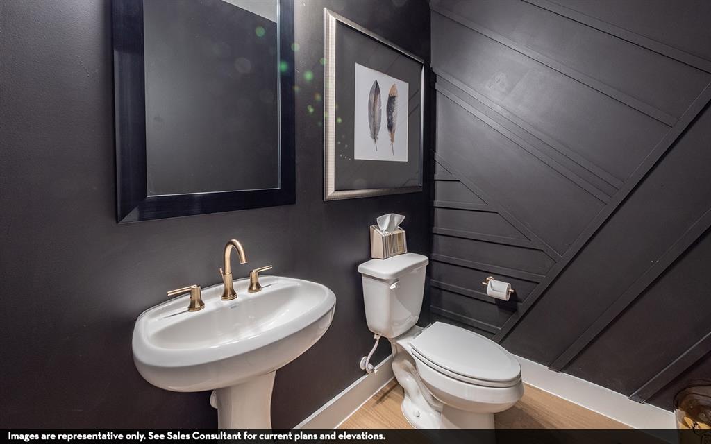 Pedestal sink with a bronze-finish faucet, dark-framed mirror, and a toilet with a paneled accent wall Pedestal sink with a bronze-finish faucet, dark-framed mirror, and a toilet with a paneled accent wall