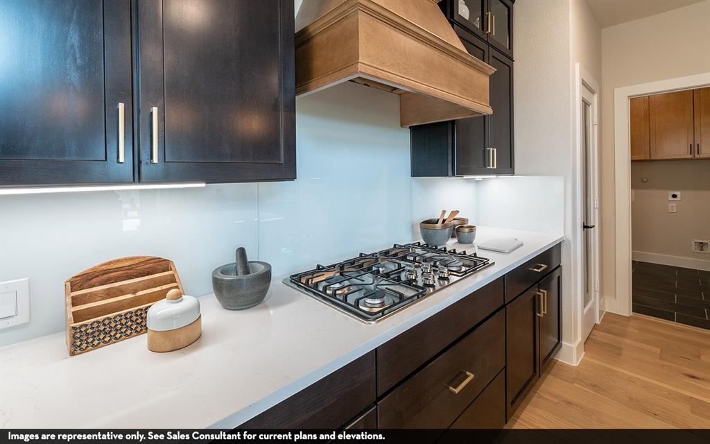 Built-in gas cooktop, wood-finish range hood, dark wood-finish cabinetry, white countertop, and under-cabinet lighting Built-in gas cooktop, wood-finish range hood, dark wood-finish cabinetry, white countertop, and under-cabinet lighting