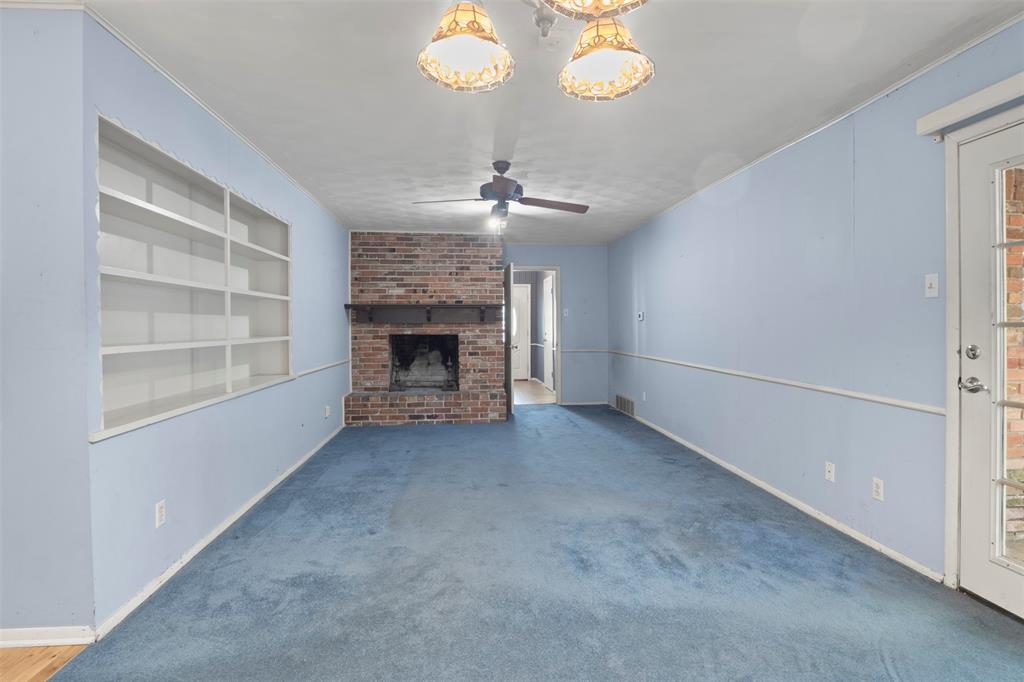 Built-in shelving, brick fireplace with mantel, ceiling fan, and decorative overhead lighting Built-in shelving, brick fireplace with mantel, ceiling fan, and decorative overhead lighting