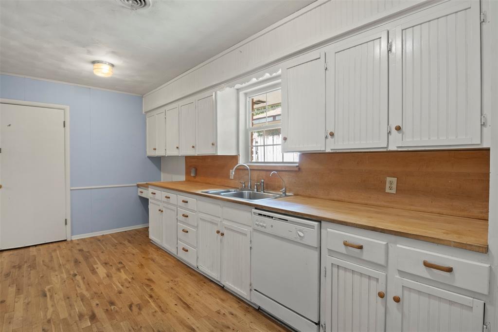 Wood-finish flooring with white beadboard cabinetry, wood countertops, and a double basin sink