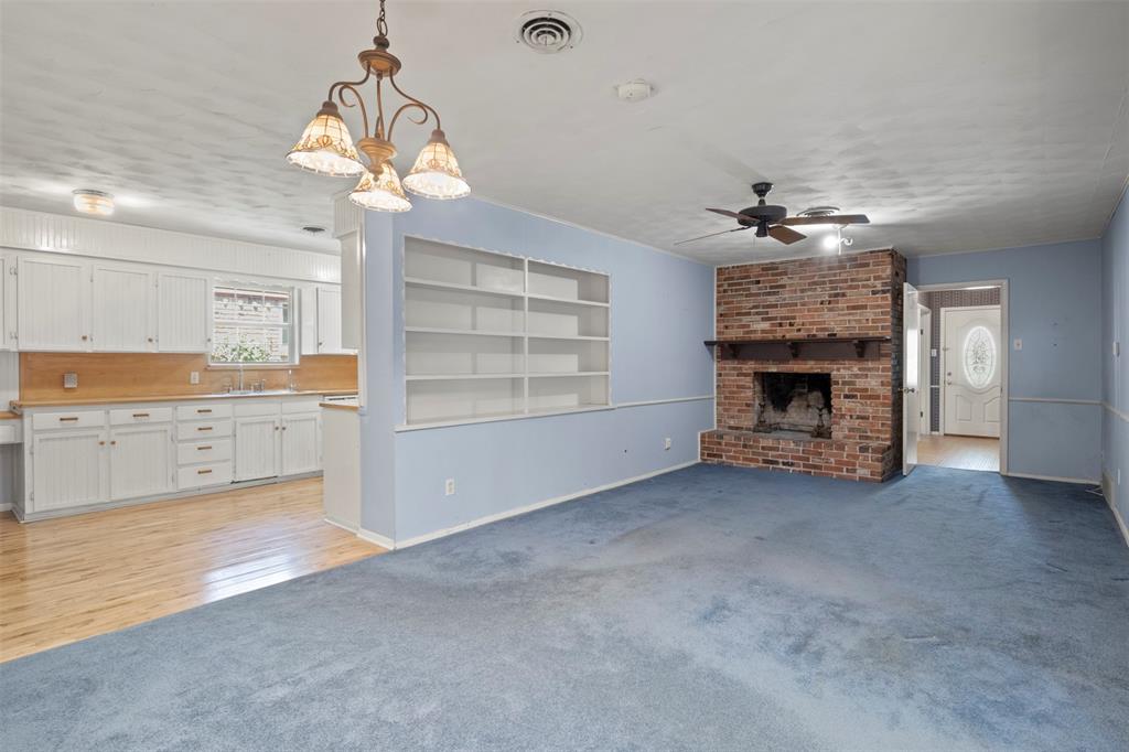 Brick fireplace with a wood mantle, built-in shelving, white cabinetry, wood-finish countertops, and wood-finish flooring Brick fireplace with a wood mantle, built-in shelving, white cabinetry, wood-finish countertops, and wood-finish flooring