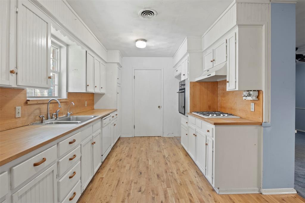 U-shaped kitchen with wood-finish flooring, white cabinetry, integrated dual basin sink, and built-in oven with gas cooktop