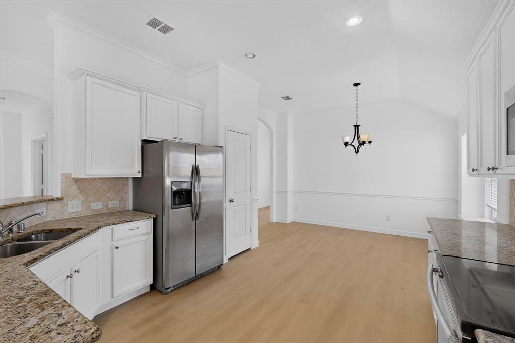 Kitchen featuring white cabinetry, stone-finish countertops, stainless steel appliances, wood-finish flooring, and vaulted ceilings with an integrated chandelier