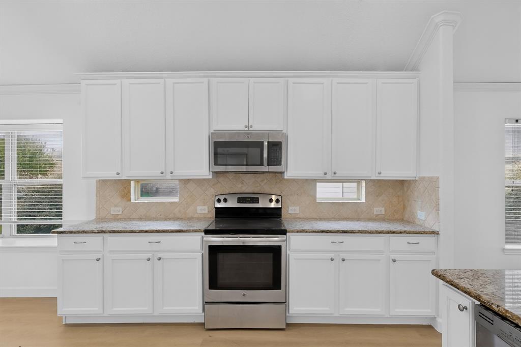 Kitchen featuring white cabinetry, stone-finish countertops, herringbone-pattern tile backsplash, stainless steel appliances, and integrated small windows