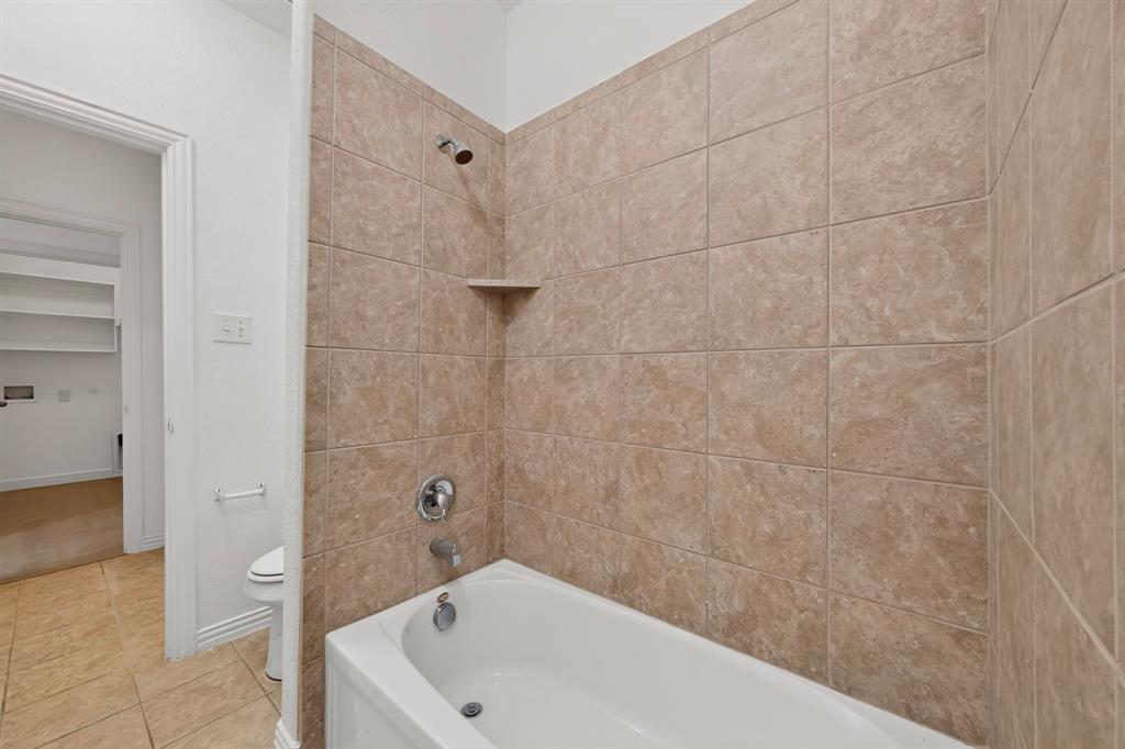 Bathtub featuring a white acrylic finish, integrated shelving, metallic fixtures, and full-height wall tile surrounds