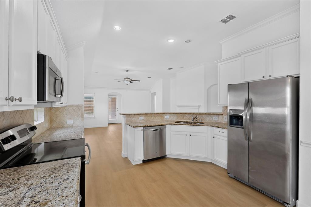Kitchen featuring white shaker-style cabinetry, stone-surface countertops, tile backsplash, stainless steel appliances, and wood-finish flooring