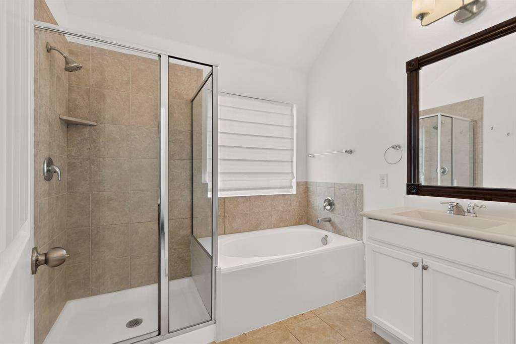 Bathroom featuring a glass-enclosed shower, built-in soaking tub with tile surround, white vanity cabinet, and vaulted ceiling