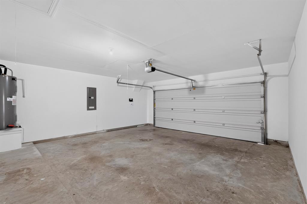 Enclosed garage featuring concrete flooring, white walls, overhead door opener, and integrated electrical panel