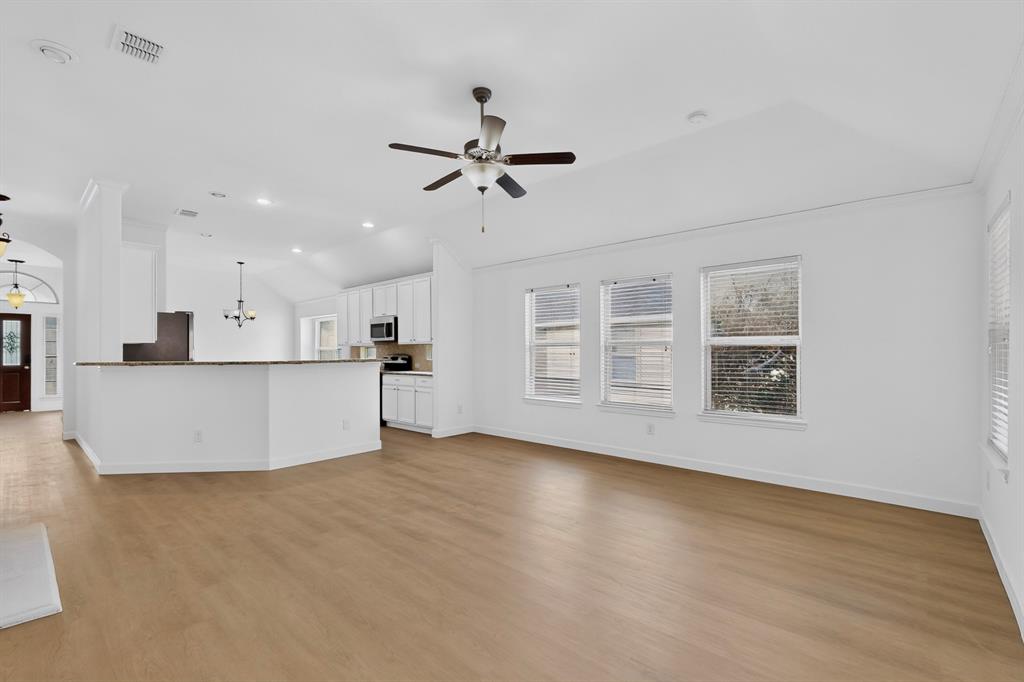 Open-concept interior featuring vaulted ceilings, wood-finish flooring, a kitchen breakfast bar, and multiple windows with horizontal blinds