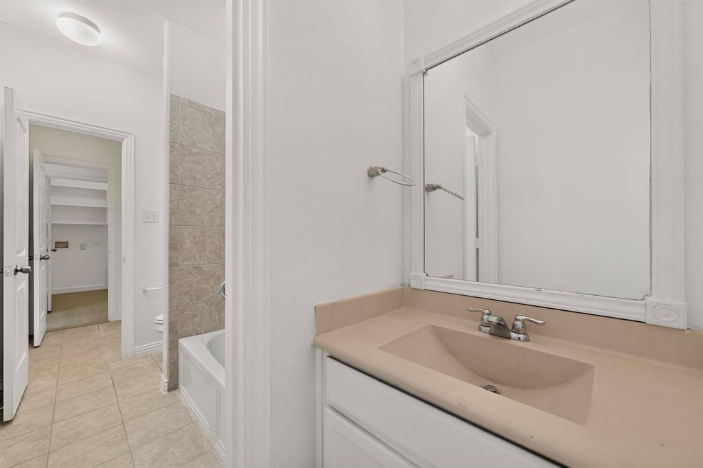 Bathroom featuring a vanity with integrated sink, framed wall-mounted mirror, ceramic tile flooring, and a bathtub with tile surround