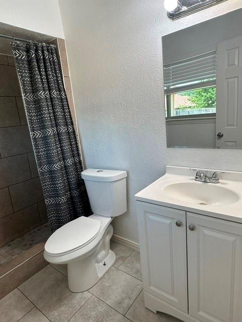 Tiled shower surround, white toilet, single vanity with integrated sink, chrome faucet, and tiled flooring