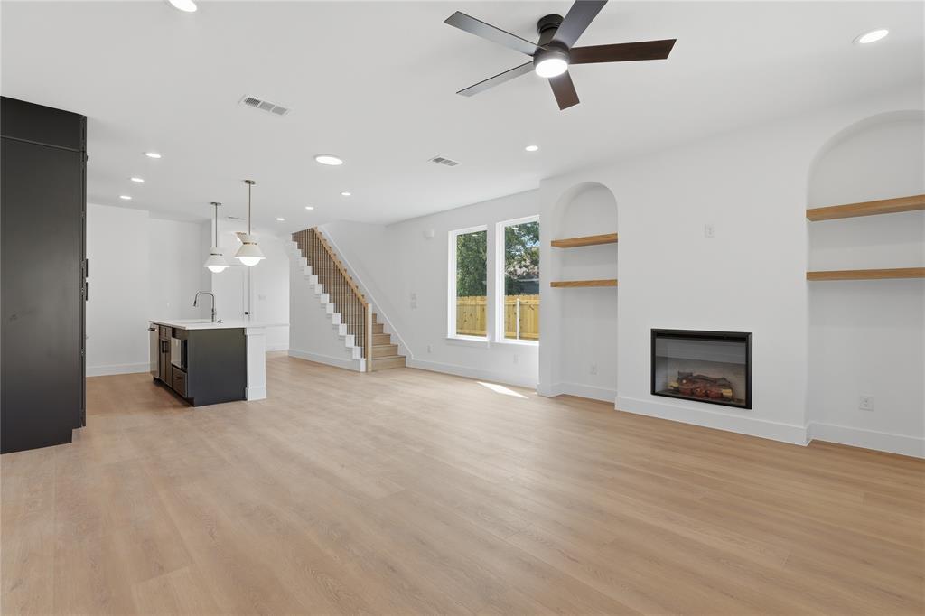 Open-concept living space with light wood-finish flooring, recessed lighting, and a modern fireplace with built-in arched shelving