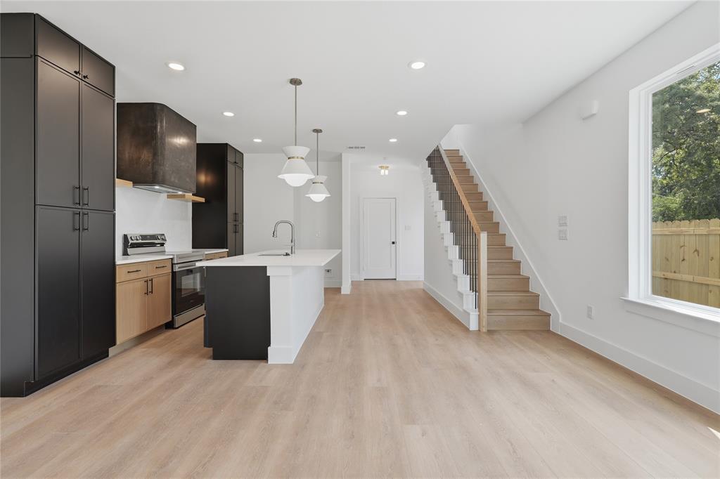 Open-concept kitchen with a white island, light wood-finish flooring, and a modern staircase featuring black spindles and a wood handrail