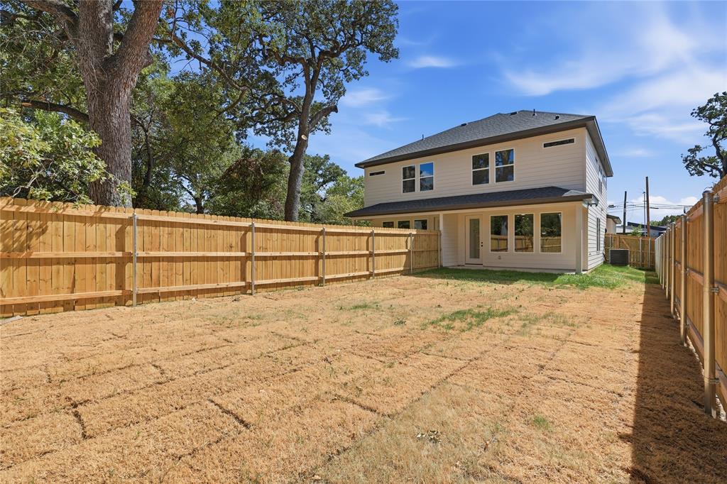 Expansive backyard with a full privacy fence, established trees, and a two-story residence featuring multiple windows and a rear entry door