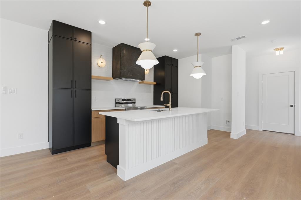 Modern kitchen featuring a large center island with fluted paneling, light wood-finish flooring, matte black cabinetry, and gold-tone pendant lighting