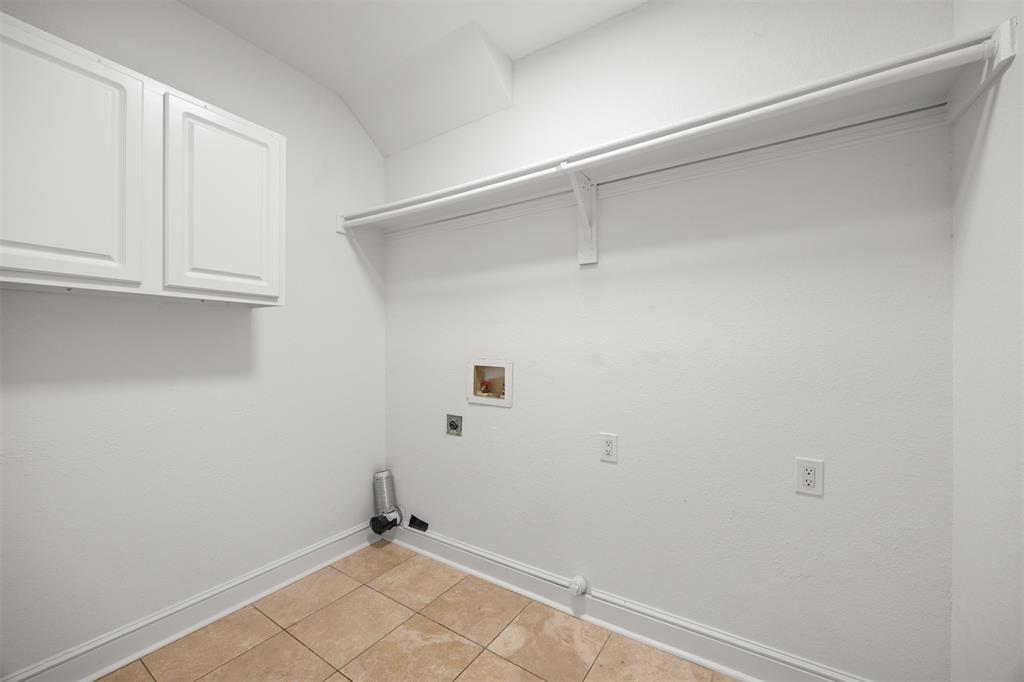 Laundry room has hookups for electric washer and dryer, shelving, cabinet, custom baseboard, and Travertine flooring.