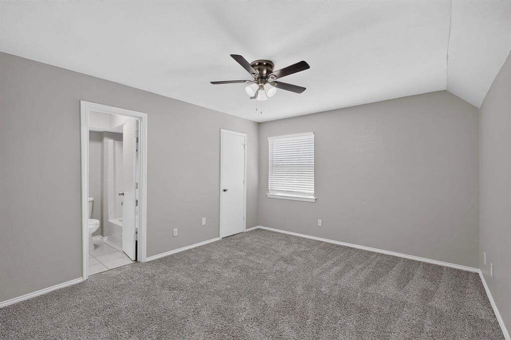 Carpeted flooring, vaulted ceiling, ceiling fan, window with blinds, and an attached bathroom with a toilet and tub
