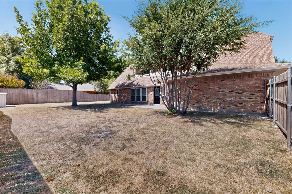 Brick exterior featuring a wood fence, mature trees, and an outdoor patio