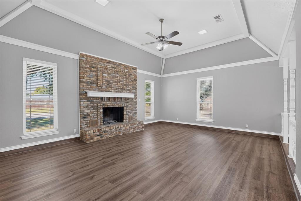 Vaulted ceiling, brick fireplace with a white mantel, ceiling fan, multiple windows, and wood-finish flooring
