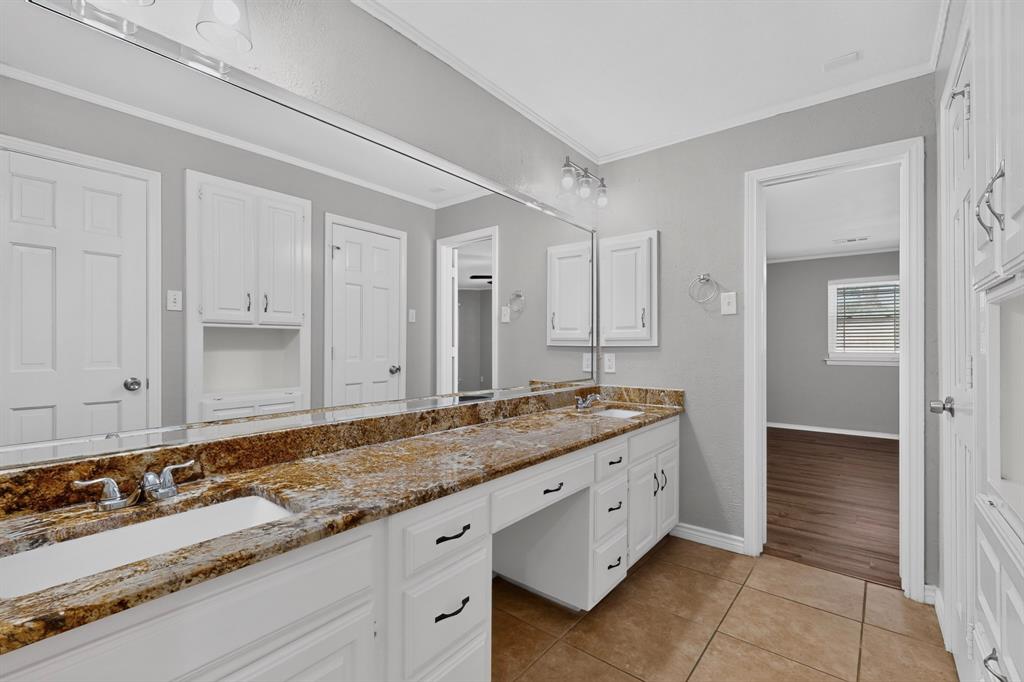 Dual sink vanity with stone-finish countertop, white cabinetry, and a full-width mirror