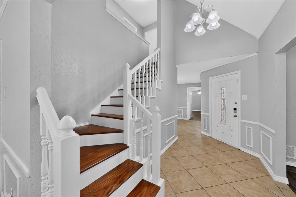 Two-story foyer featuring a staircase with wood-finish treads and white risers, white balusters, and a white newel post Two-story foyer featuring a staircase with wood-finish treads and white risers, white balusters, and a white newel post