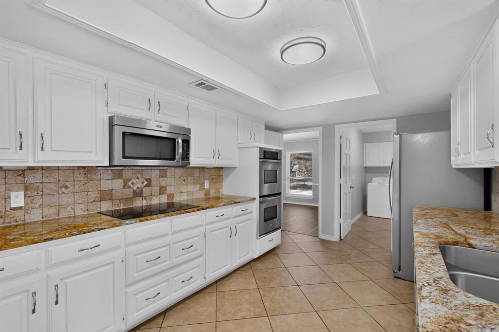 White cabinetry, granite countertops, tile backsplash, built-in stainless steel appliances, and tile flooring