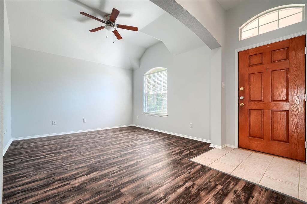 Vaulted ceiling featuring a ceiling fan, wood-finish flooring, arched window with blinds, panel-style entry door, and tile flooring