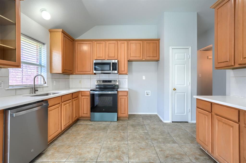 Kitchen featuring wood cabinetry, stainless steel appliances, white countertops, a tile backsplash, and tile flooring