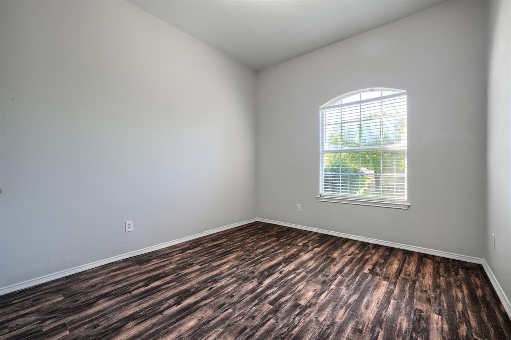 Arched window with blinds, wood-finish flooring, and light-toned walls