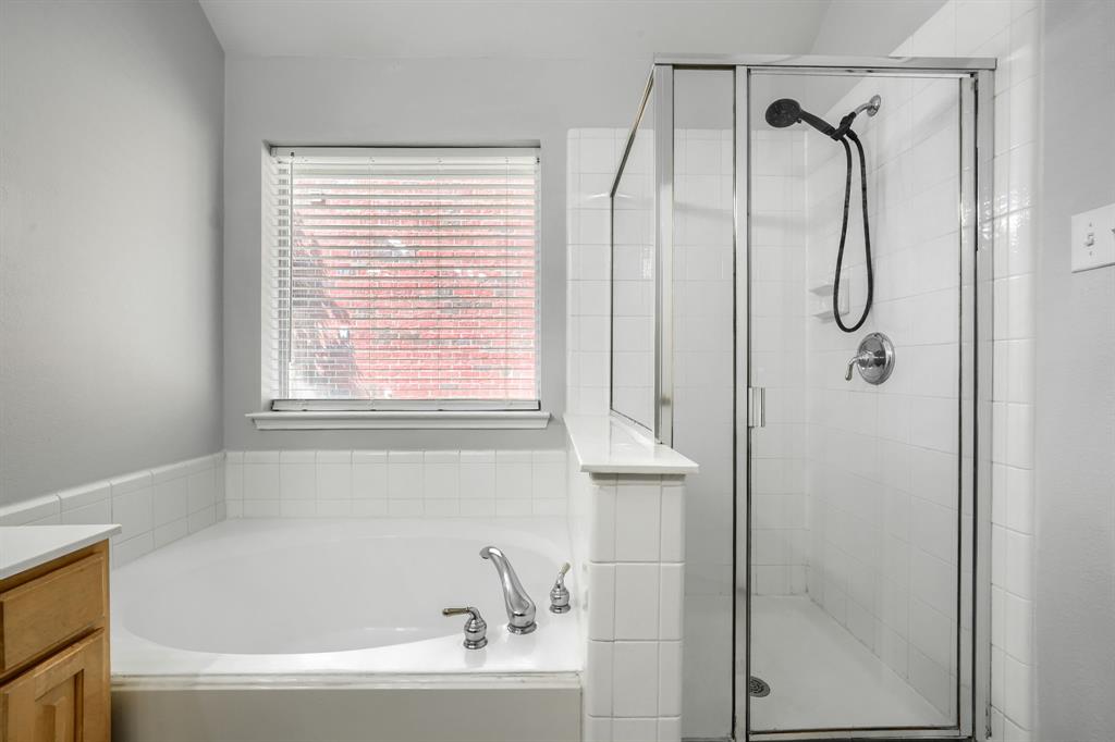Built-in soaking tub with chrome fixtures, glass-enclosed shower with tile surround, and light wood-finish cabinetry