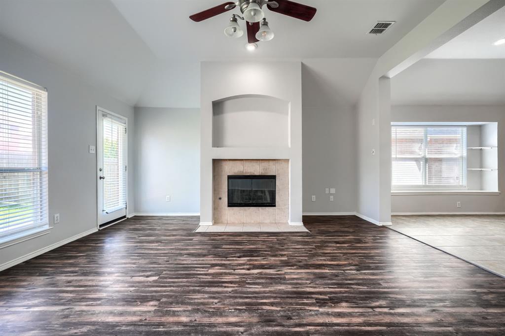 Spacious living area featuring wood-finish flooring, a ceiling fan with integrated lighting, and a tiled fireplace with an arched niche