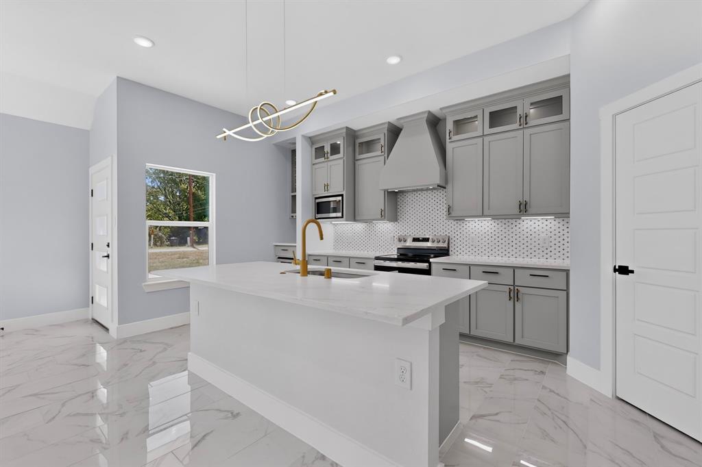 Kitchen featuring a central island with a countertop, gray cabinetry, stainless steel appliances, a honeycomb tile backsplash, and a modern light fixture