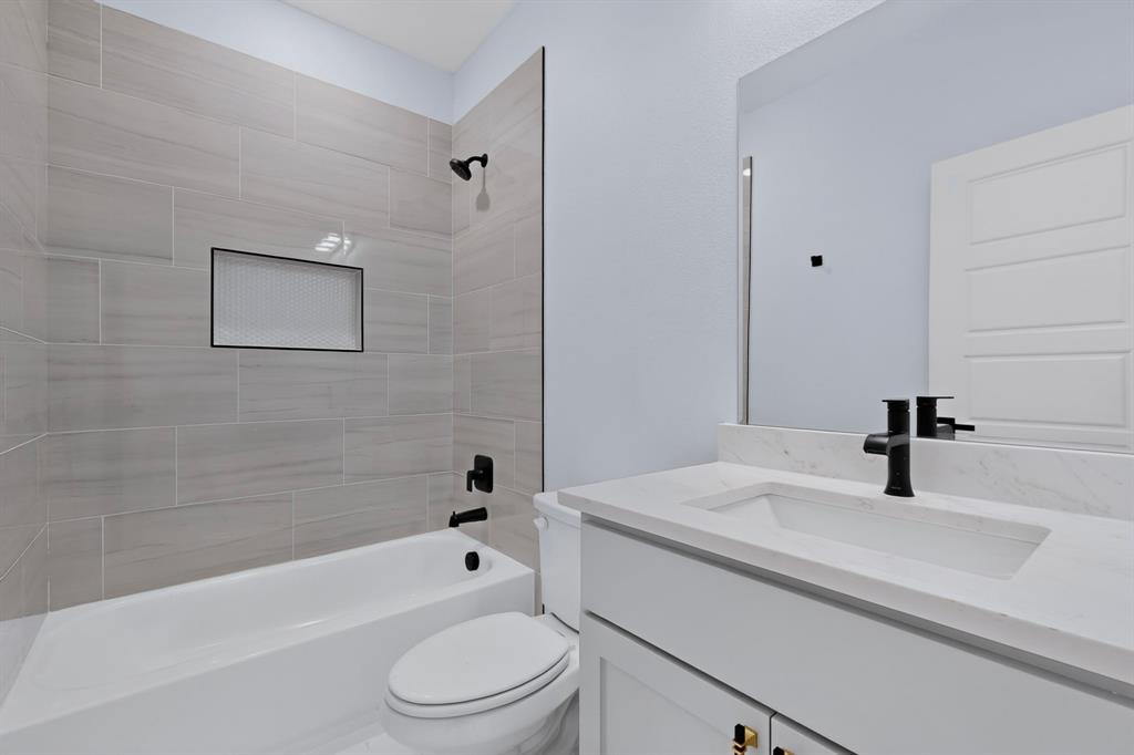 Bathtub with light-toned tiled surround, integrated shower niche, and matte black fixtures